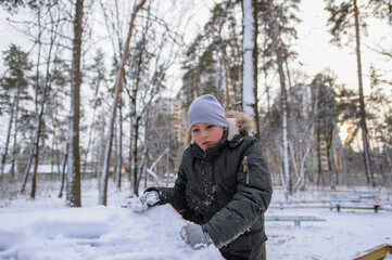 Fototapeta na wymiar cute white boy in a warm coat and hat plays with snow on the playground in the park in winter