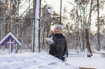 Fototapeta na wymiar ittle boy in warm winter clothes throws a snowball in a winter park and smiles