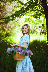 Portrait of young woman in blue dress in spring garden with a basket full of lilacs. Spring background. Woman's Day. Greeting card. 