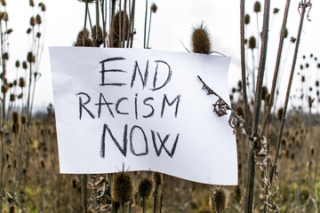 End Racism Now- message written on a paper stuck in dry vegetation, thorns. Concept- racism
