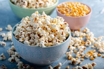 Salty popcorn in a blue bowl  with corncobs on the blue background.