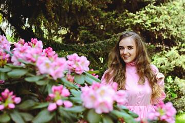 Portrait of young attractive woman in spring garden with blooming pink flowers. Spring background. Woman's Day. Greeting card. 