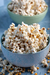 Salty popcorn in a blue bowl  with corncobs on the blue background.