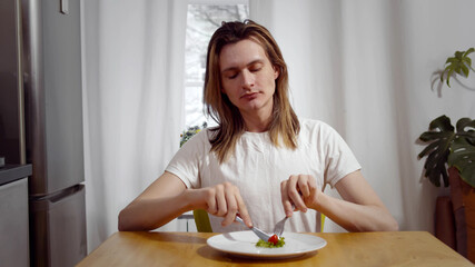 Young man sitting on chair and eating tomato and salad on plate.