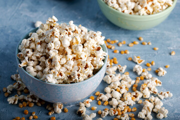 Salty popcorn in a blue bowl  with corncobs on the blue background.