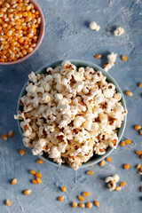 Salty popcorn in a blue bowl  with corncobs on the blue background.