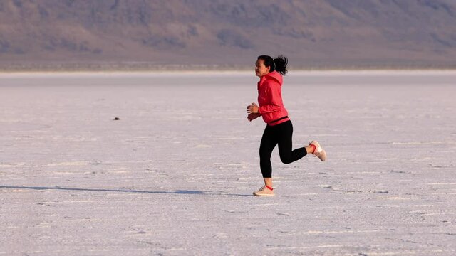 Asian woman jogging across the Bonneville Salt Flats flats in Utah. Slow Motion.