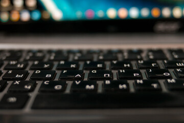 Laptop keyboard. The display is blurred. Bright laptop. White letters and black keys. Gray computer. Digital technologies.