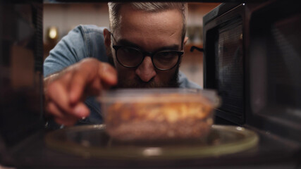 Man putting leftover dinner into microwave oven to cook - obrazy, fototapety, plakaty