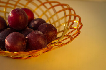 Several ripe plum lie in a braided tray