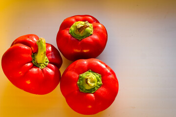 Several juicy red bell peppers lie in the rays of the sun