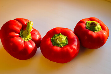 Several juicy red bell peppers lie in the rays of the sun