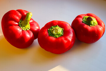 Several juicy red bell peppers lie in the rays of the sun