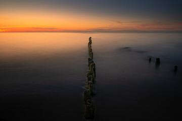 Sunset at the Baltic Sea. Wooden breakwater on the horizon