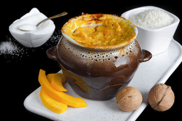 Sweet rice porridge with pumpkin and nuts, baked in a ceramic pot, black background. Selective focus