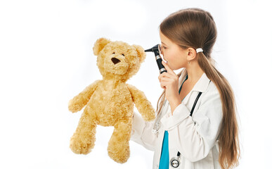 Caucasian girl playing with her patient plush bear in a doctor game. Child using ophthalmoscope