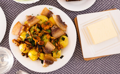 baked potatoes with chanterelles and bacon served with herbs on white plate. top view