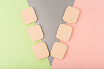 Creative V-type arrangement of make up sponges on light green, silver and pink background. Concept of visage art and make up application