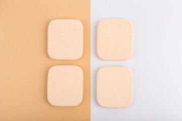Flat lay with four square shaped make up sponges on beige and white background. Concept of beauty and make up