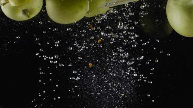 Halves of green apples in water. Action. Juicy green apples fall into water with bubbles on black background. Refreshing water with green apples