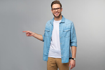Fototapeta premium Happy young handsome man in jeans shirt pointing away standing against grey background