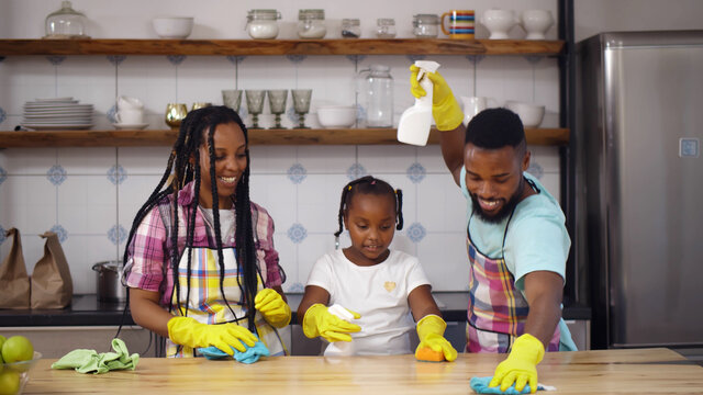 Happy African Family In Apron And Rubber Gloves Cleaning Kitchen Surface Together