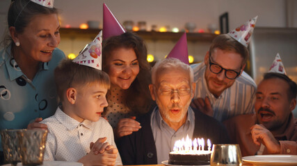 Gathering of friends and family at birthday party for senior man blowing out birthday candles.