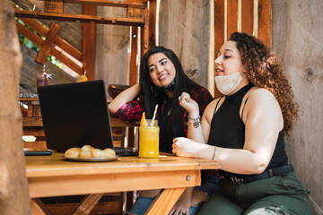 Women sitting at a bar enjoying a juice - Two women wearing masks sitting at a bar working on a laptop .