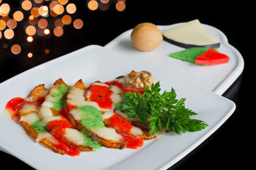 Fried pumpkin slices with multicolored melted cheese, herbs and nuts on a plate, black background. Selective focus