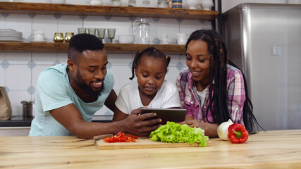 Happy black family reading vegetarian recipe on tablet pc cooking together in kitchen