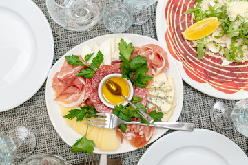 Festive table setting, family dinner with served italian antipasti - marinated salmon, hamon, Carpaccio, pear, basil. Tablescape.