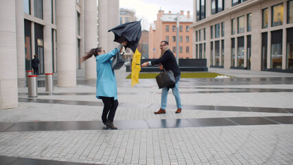 Businessman and businesswoman in coat shelter umbrella from the rain and strong wind outside