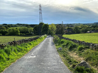 View along, Hallas Lane, with dry stone walls, fields and trees, on a cloudy day in, Queensbury, Bradford, UK