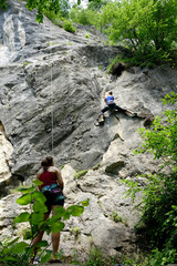 LOW ANGLE: Belayer looks after fit female climber climbing a towering cliff.