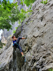 VERTICAL: Nimble Caucasian woman top rope climbs up a towering rocky wall.