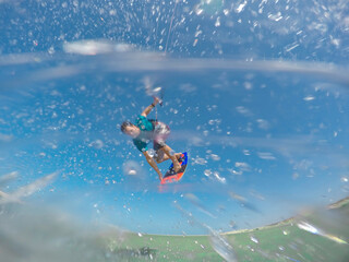 CLOSE UP: A flurry of water droplets fly towards camera as fit man kitesurfs.