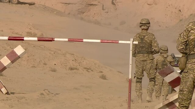 A military patrol stops a car at a checkpoint in a desert war zone.