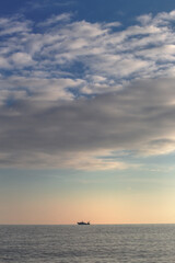 Vertical seascape view of a boat in the distance at dusk light, dominated by clouds, Liguria, Italy.
