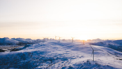 Wind turbines on snowy ridges at glowing sundown