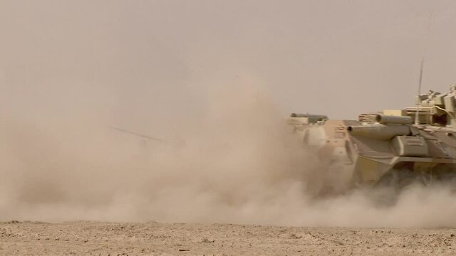 An armored personnel carrier drives through the sand in the desert, raising a cloud of dust. Concept: war zone in the east, movement of military equipment.