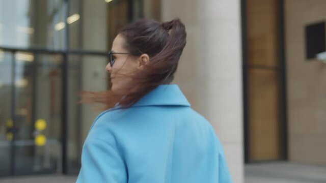 Elegant young businesswoman in blue coat entering office building