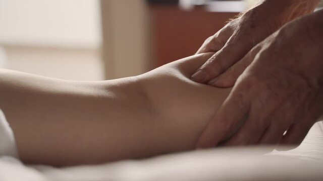 Relaxing leg massage with hands applying pressure on calf muscles in clinic. Close up on male therapist hands performing pain and stress relief treatment on female leg lying in massage bed or table