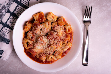 Cooked Italian Tortellini in Red Tomato Sauce with Cheese In White Bowl on Marble Surface with Graphic Napkin