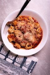 Cooked Italian Tortellini in Red Tomato Sauce with Cheese In White Bowl on Marble Surface with Graphic Napkin