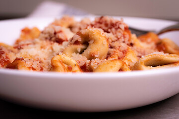 Cooked Italian Tortellini in Red Tomato Sauce with Cheese In White Bowl on Marble Surface with Graphic Napkin