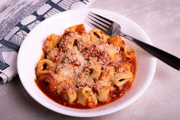 Cooked Italian Tortellini in Red Tomato Sauce with Cheese In White Bowl on Marble Surface with Graphic Napkin