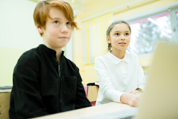 A girl in a white shirt and a boy in a black sweater study online using a computer