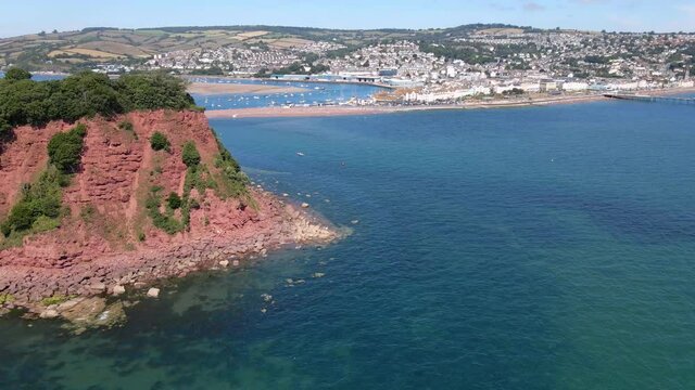 Aerial orbiting shot of ness cove cliffs and babbacombe bay during sunny day with blue sky in Shaldon,England. Beautiful landscape with Shaldon City and Harbor on hill.