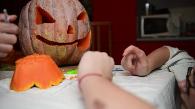 4K Father and daughter carving pumpkin, Jack o lanterns on Halloween in the kitchen. Celebrating Halloween at home with a Creepy Pumpking, fall family tradition