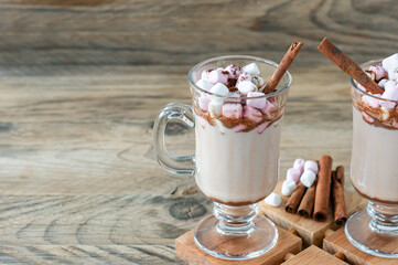 Hot cocoa or chocolate drink with marshmallow in glass mug on wooden table. Concept of cosy Christmas and New Year holidays, copy space